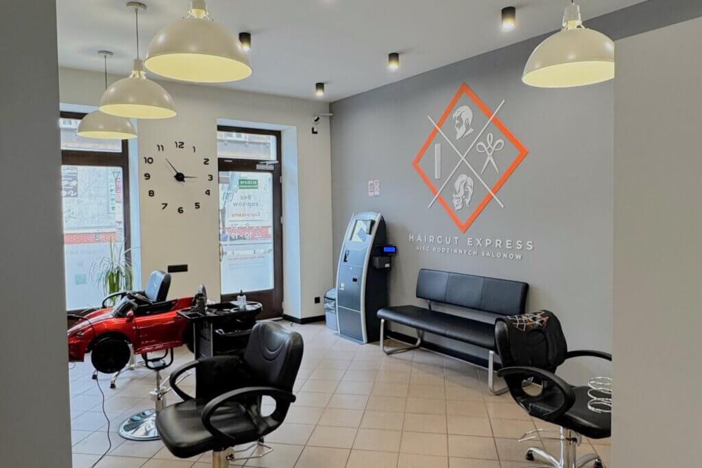 Wnętrze salonu fryzjerskiego Haircut Express na Wildzie w Poznaniu, ul. Traugutta 28/3b – stanowiska, terminal i fotelik dla dzieci